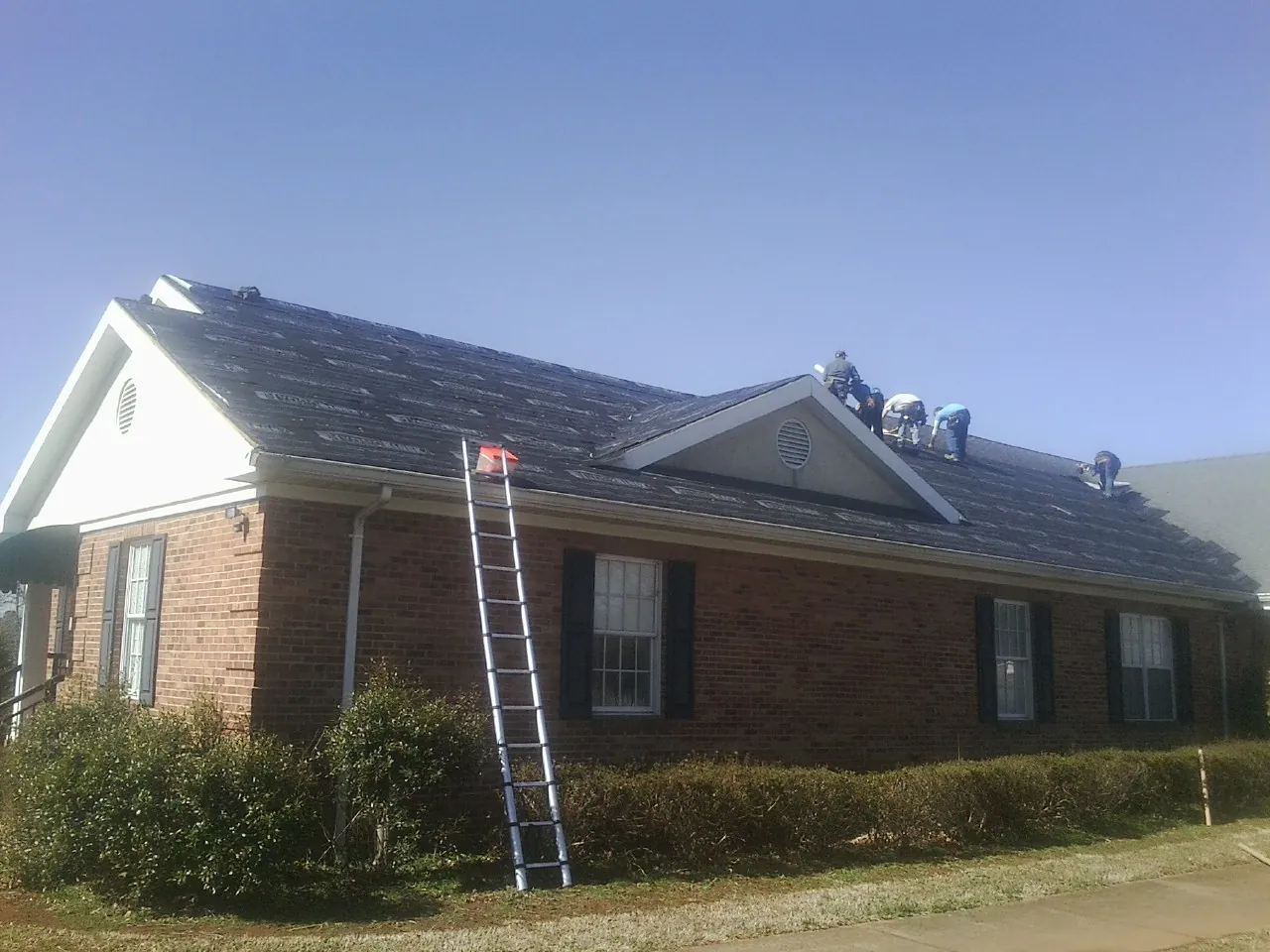 Crew tearing shingles off a brick ranch roof with a ladder set — Metal Roof Repair work by our crew in West Milford