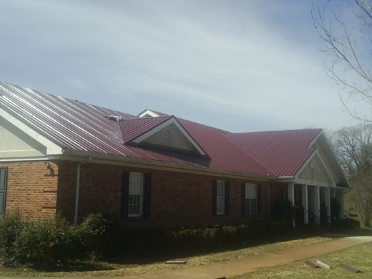 Red metal roof with gabled entries on a long brick building, from a Hail Damage Roof Repair job in West Milford