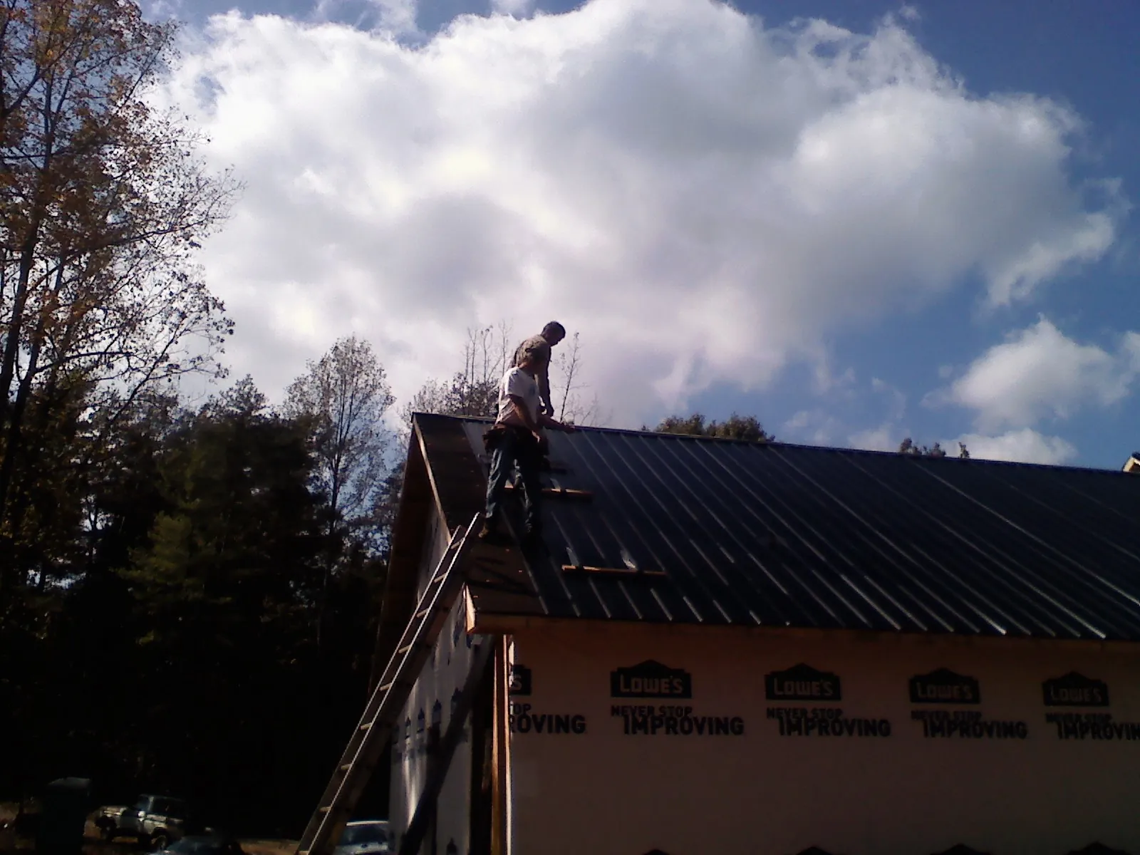 Roofer fastening dark metal panels high against a cloudy sky, from a Roof Inspection job in West Milford