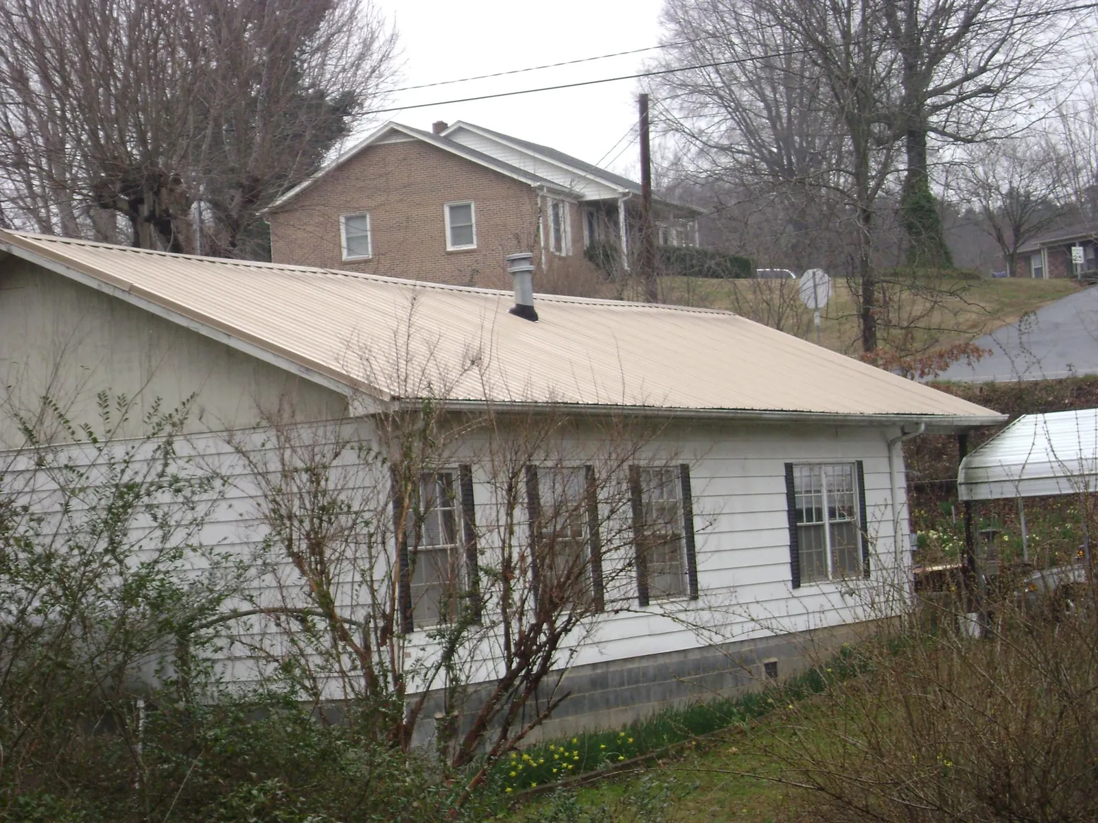 Tan metal roof on a white sided house set into a hillside — Commercial Roofing by Roofing Brothers in West Milford
